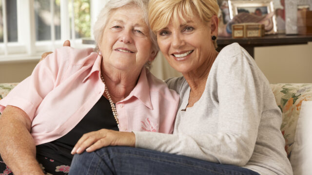 Adult Daughter Visiting Senior Mother Sitting On Sofa At Home